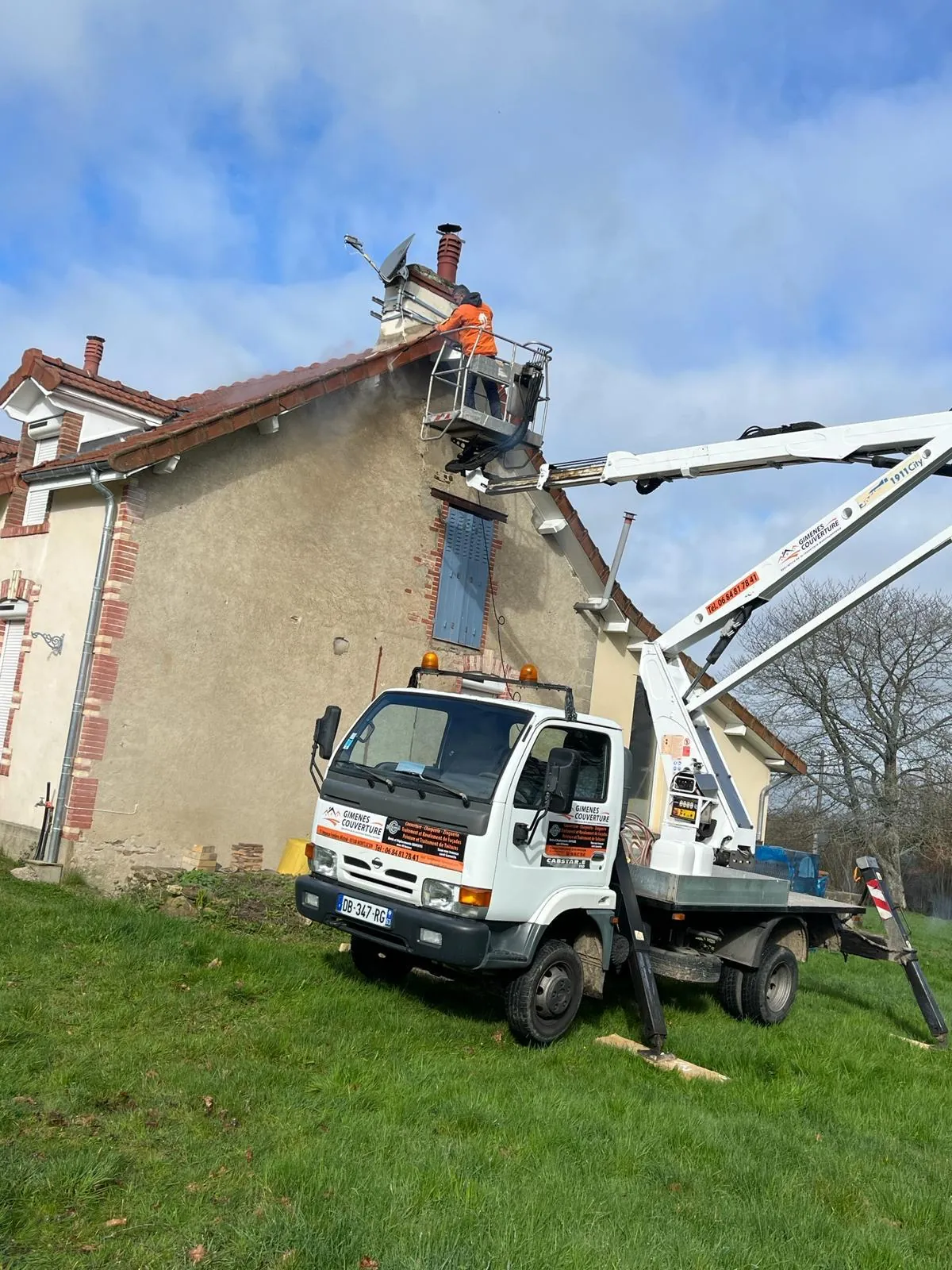 Camion nacelle au pied du pignon, un compagnon au travail à hauteur de la cheminée